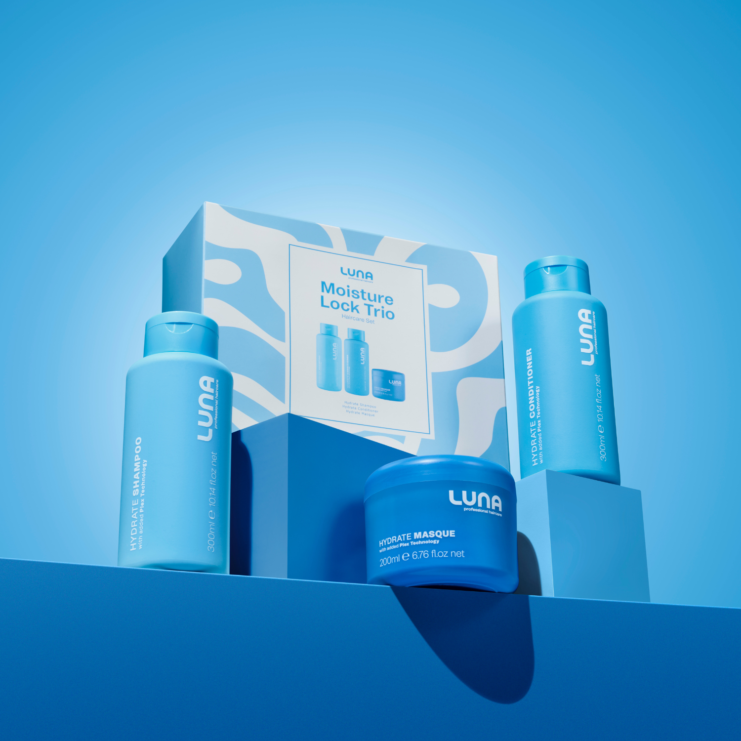 Luna Moisture Lock Trio haircare set packaging on a blue and white abstract background - holiday gift set 2025 - hydrate shampoo, hydrate conditioner and hydrate masque